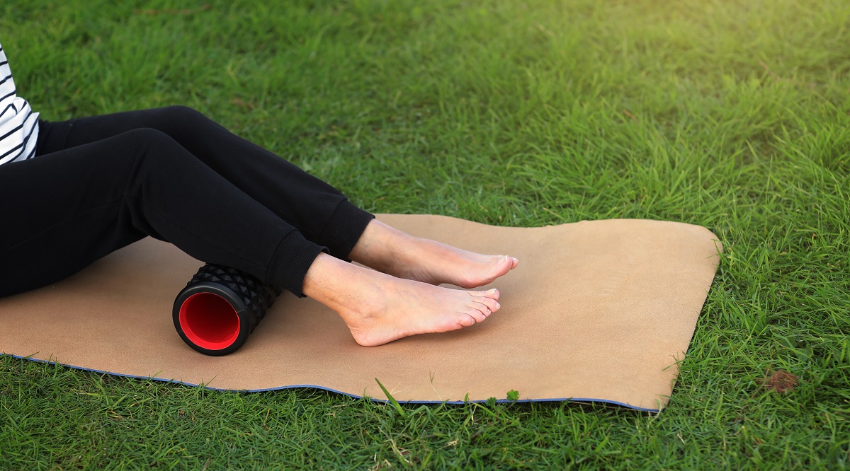 woman warms up and works out the fascia of the calf muscles with a sport massage foam roller outdoors